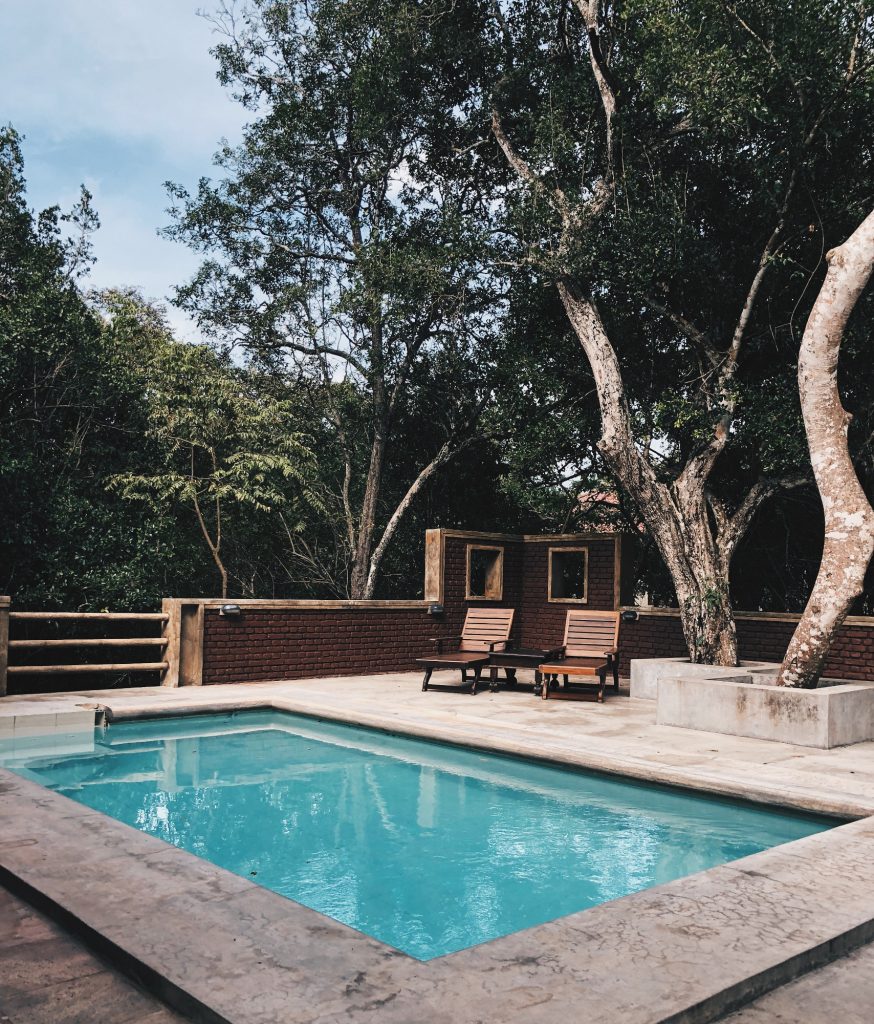 piscine en extérieur avec terrasse en béton et transats en bois sous des arbres